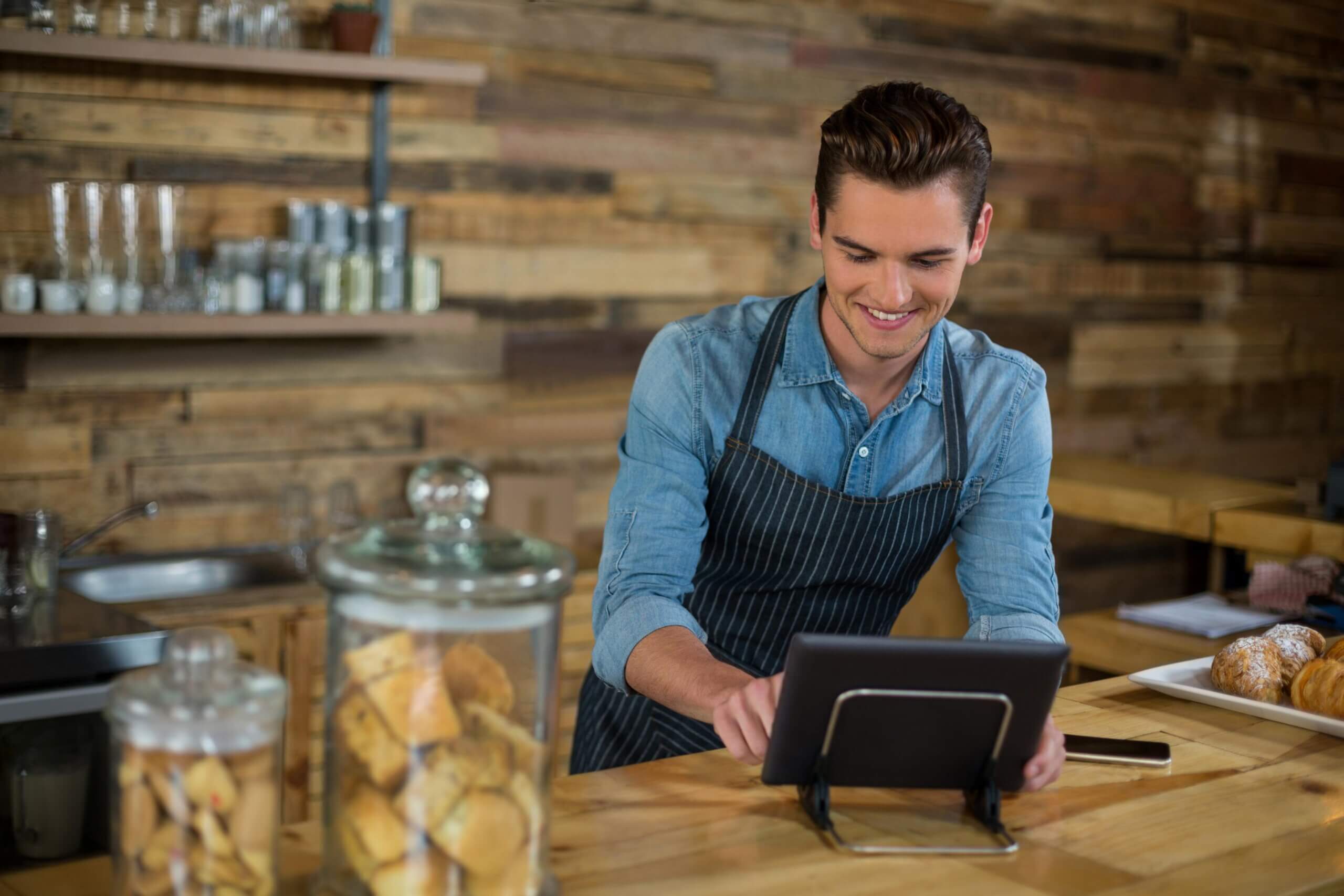 Smiling waiter using a digital tablet with a cloud-based POS system at the counter, demonstrating easy setup without the need for bulky hardware