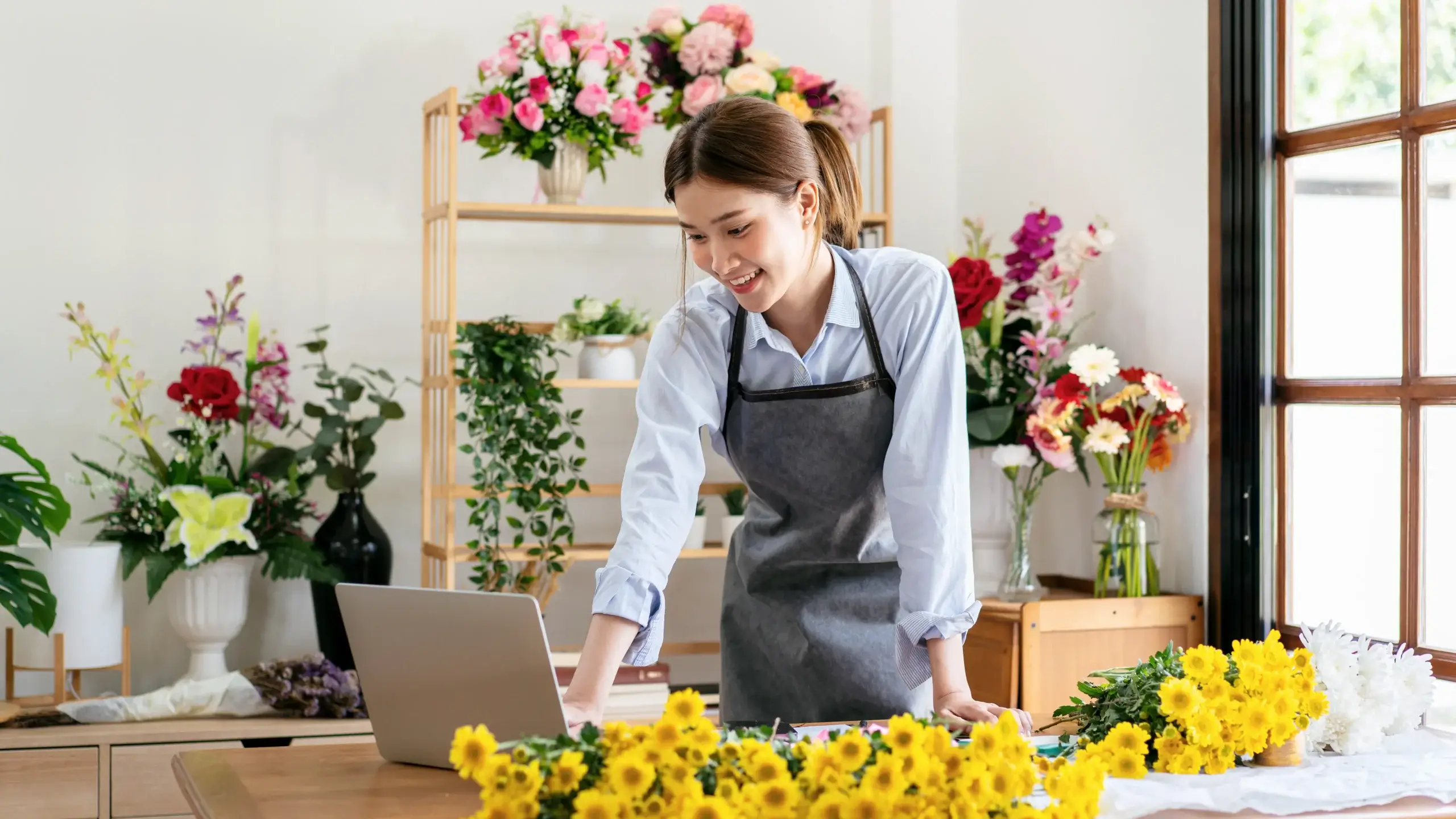 Retail - flower store owner reviewing business performance and sales data on a laptop