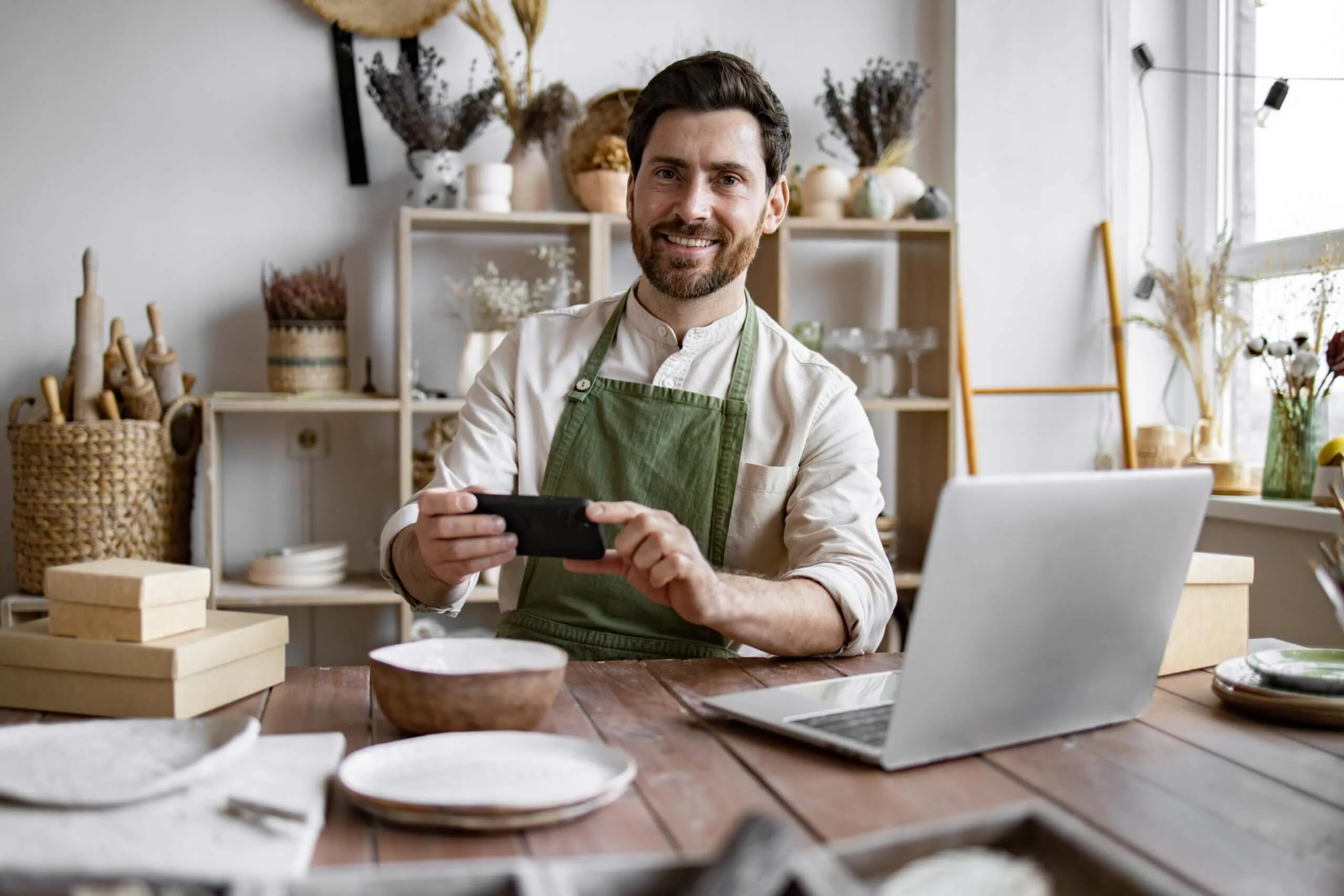 A man wearing an apron is seated at a table, focused on his phone in a relaxed setting