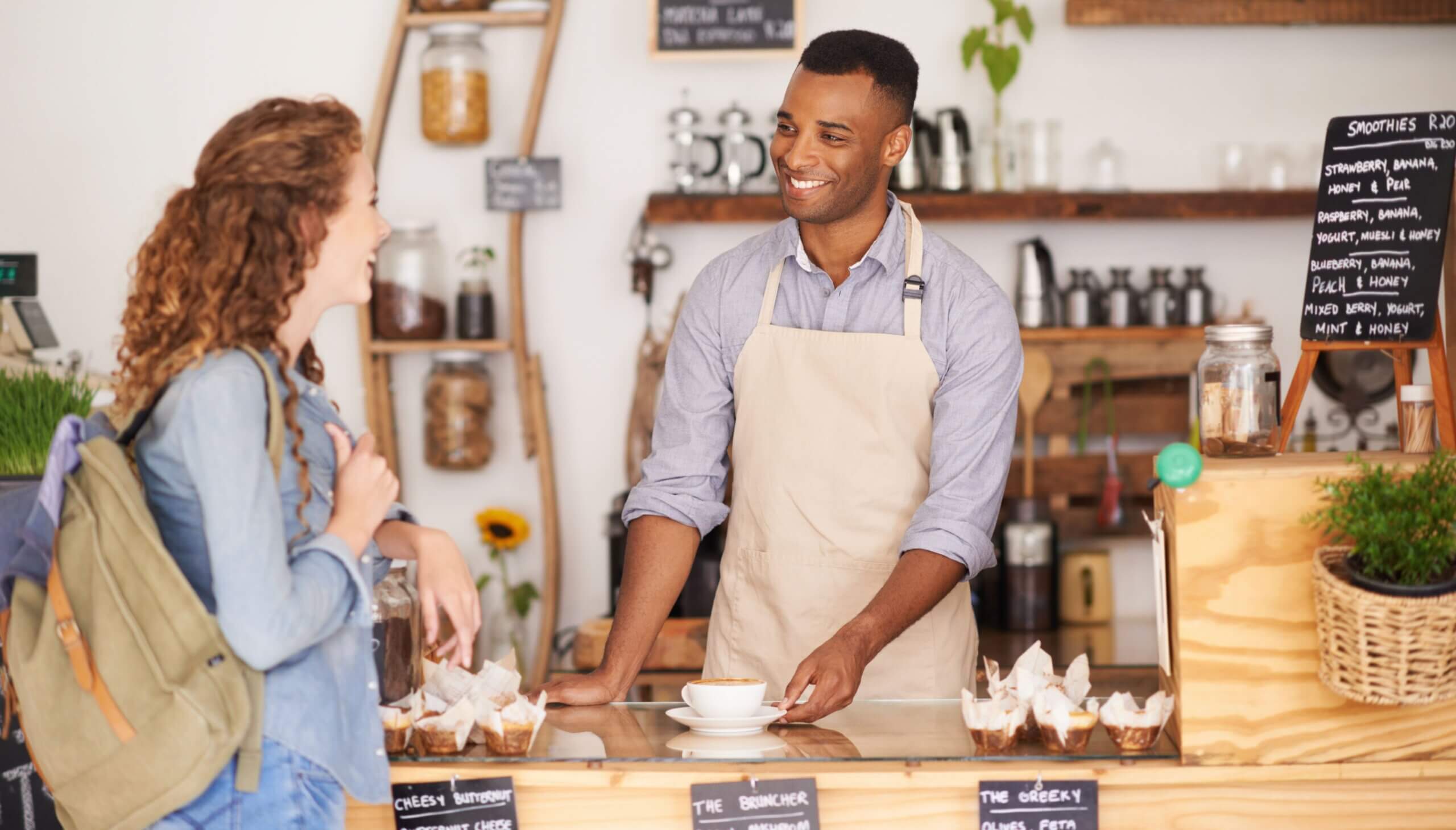  A male cashier and female customer stand together at a coffee shop, engaging at the point of sale of a small business