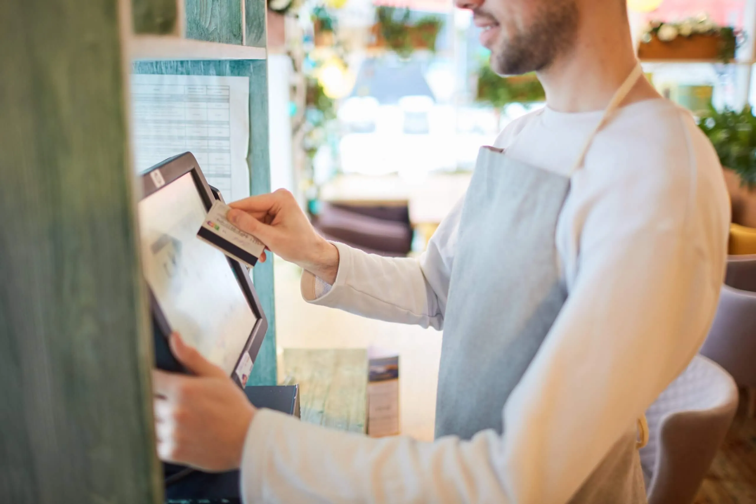 A man wearing an apron engages with a POS terminal, processing sales