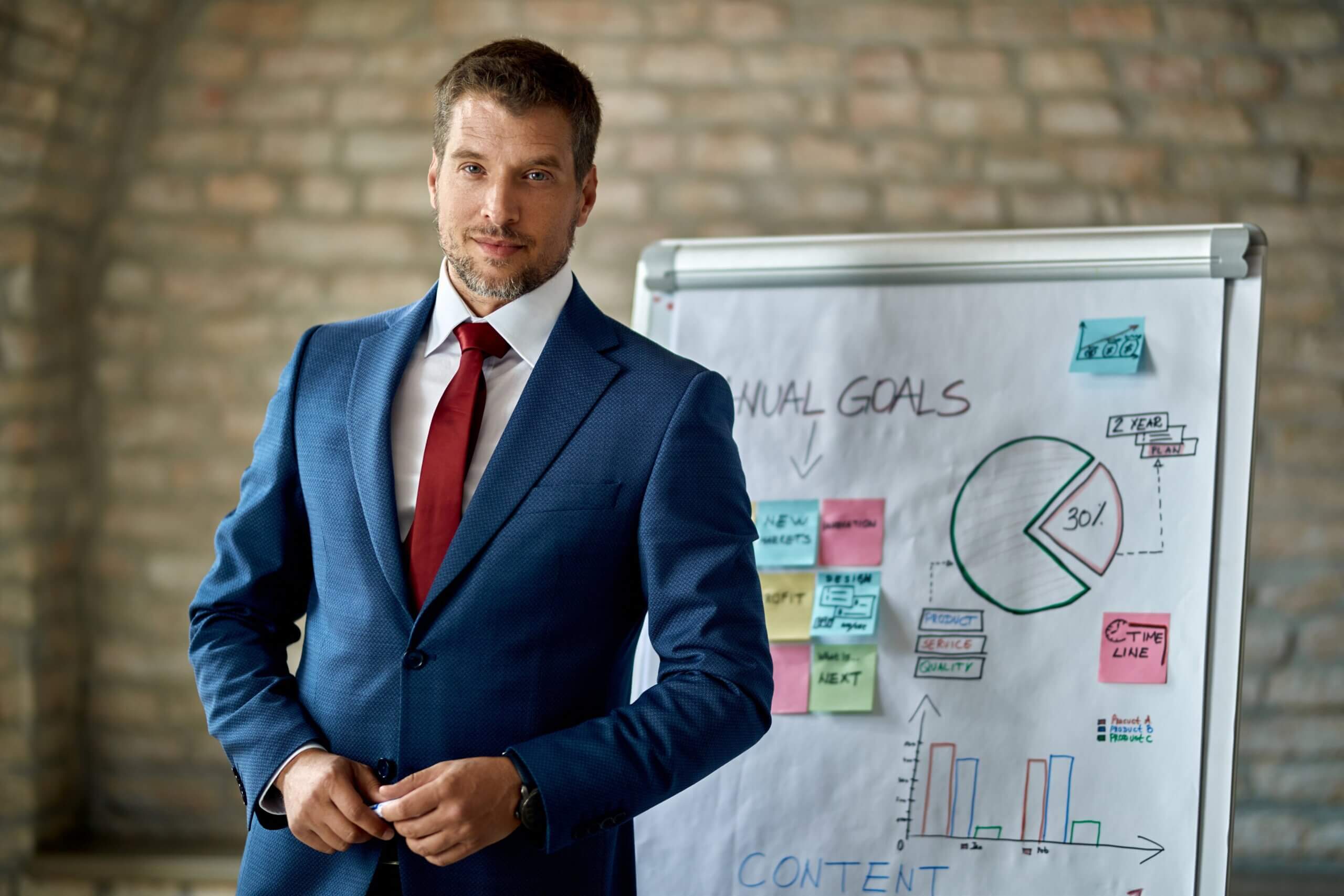 A man in a suit stands beside a whiteboard, engaged in a discussion or presentation