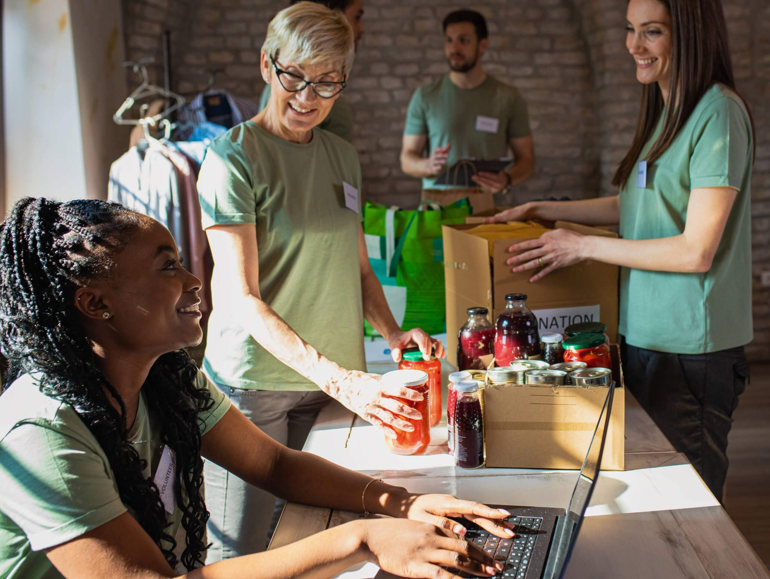 A group of individuals collaborating on laptops and sorting boxes, engaged in community donation efforts for a small business