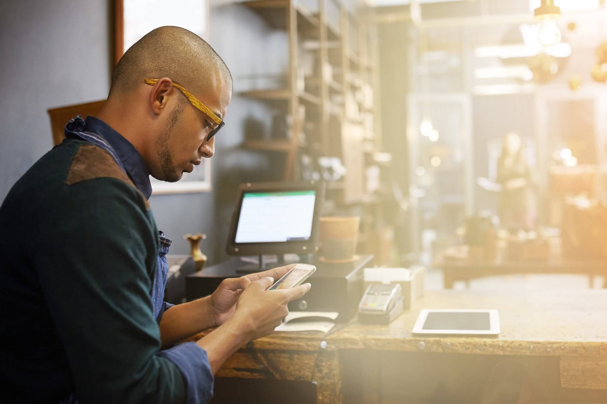A man wearing glasses is focused on his phone, exploring small business trends