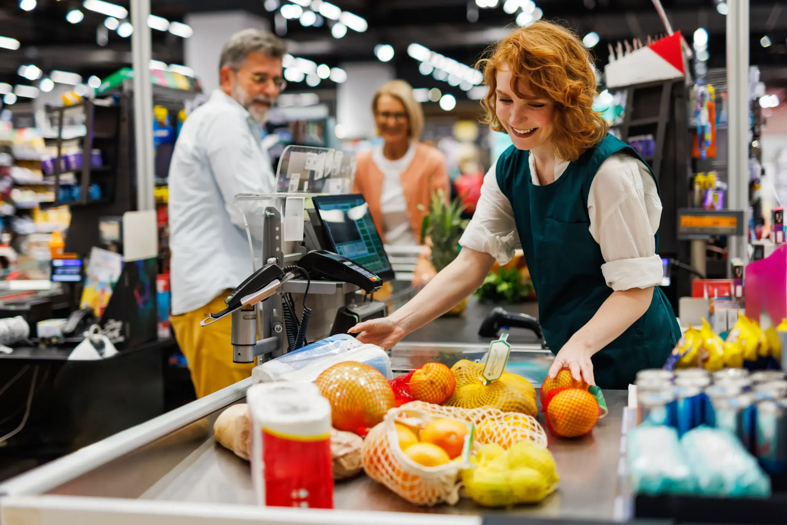 Grocery store staff assisting customer during checkout using POS system